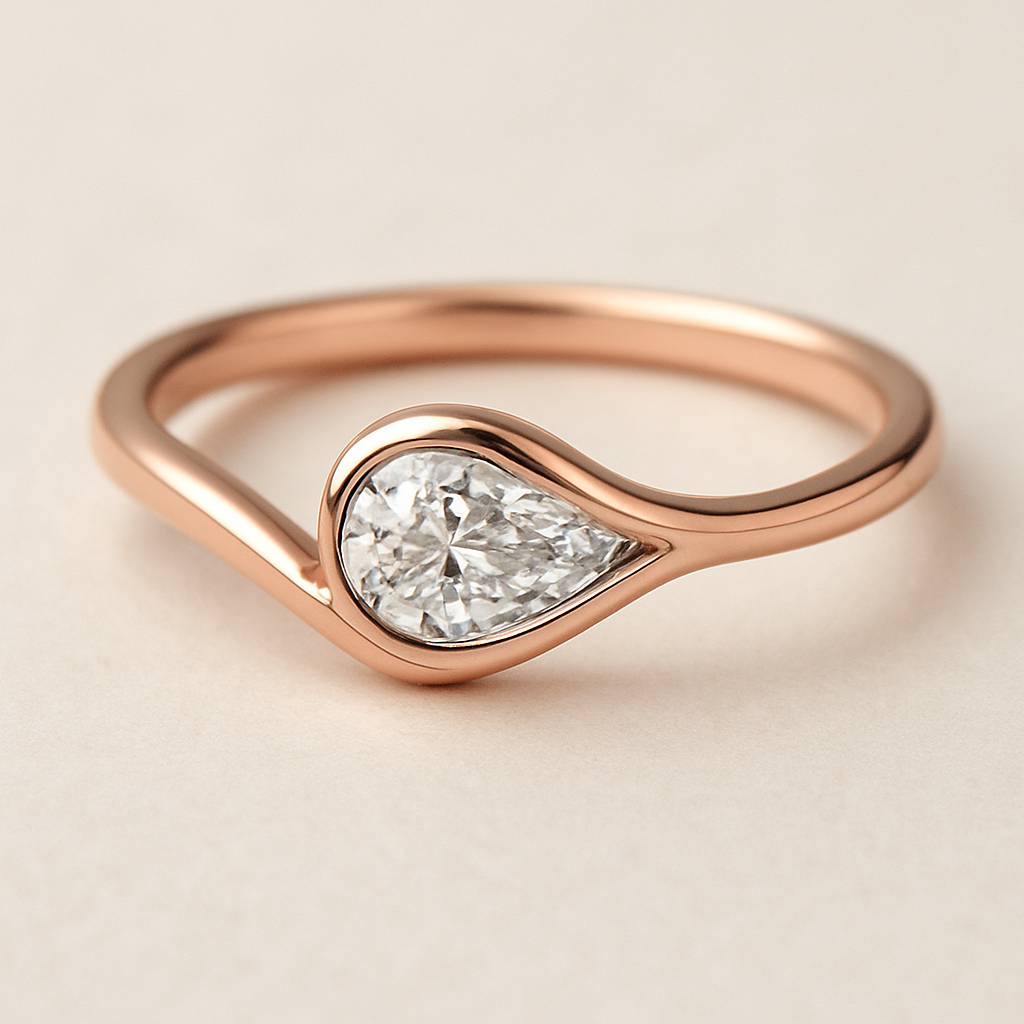 A delicate rose gold pinky ring featuring a 0.50-carat pear-shaped diamond set in a smooth bezel setting. The diamond is gently tilted to the left, creating a soft paisley-inspired curve that radiates feminine Yin energy — graceful, flowing, intuitive, and serene. The polished rose gold band enhances the gentle movement and balance of the design, symbolizing elegance, emotional depth, and the beauty of lunar energy.  