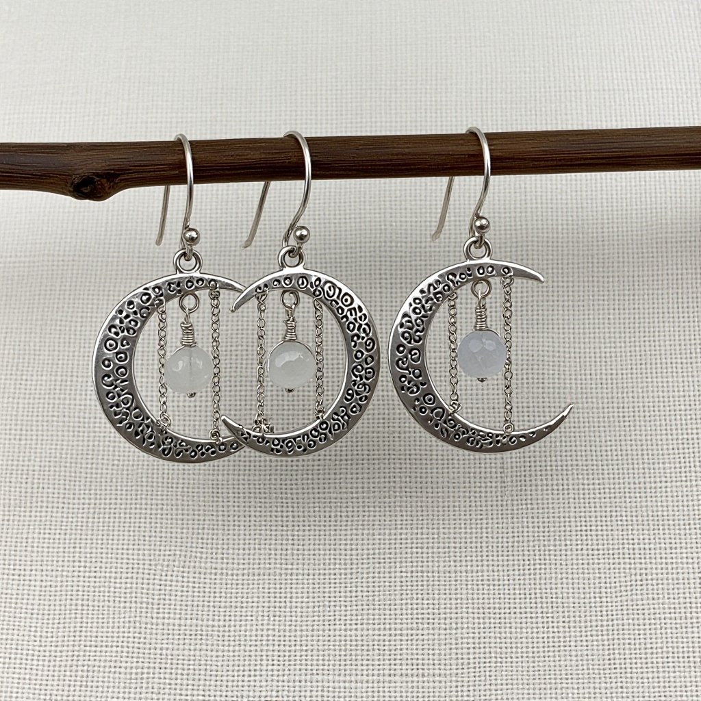 Серебряные серьги словно мятое сер ебро в форме полумесяца. Верхушка полумесяца крепится к застежке серьги.  От полумесяца идет три цепочки, у каждой на конце мелкий камушек лунный камень