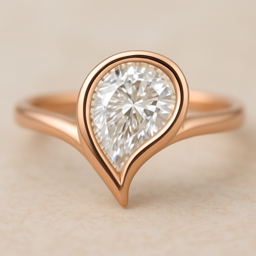 A refined and elegant rose gold ring featuring a pear-shaped diamond set in a smooth bezel setting. The diamond is tilted slightly to the side, creating a paisley-inspired shape reminiscent of a graceful flowing droplet. The rose gold band is sleek and polished, complementing the organic, curving silhouette of the stone. The design blends modern minimalism with a subtle artistic twist inspired by the Bandana paisley motif.