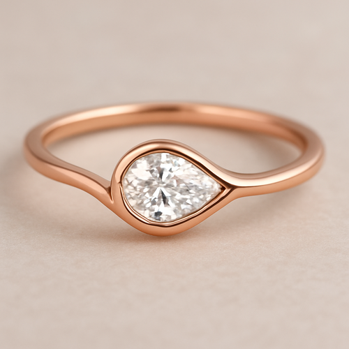 A delicate rose gold pinky ring featuring a 0.50-carat pear-shaped diamond set in a smooth bezel setting. The diamond is gently tilted to the left, creating a soft paisley-inspired curve that radiates feminine Yin energy — graceful, flowing, intuitive, and serene. The polished rose gold band enhances the gentle movement and balance of the design, symbolizing elegance, emotional depth, and the beauty of lunar energy.  