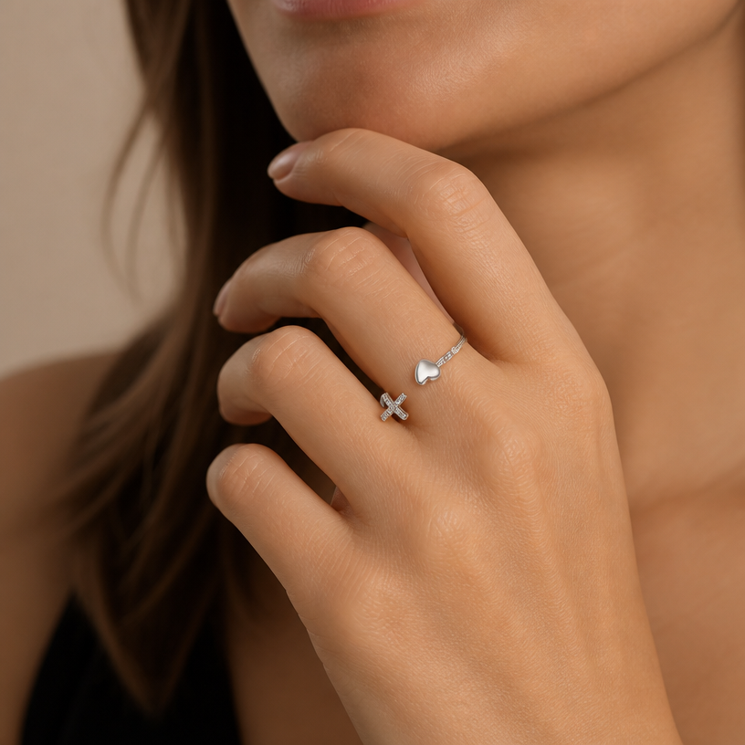 Jewelry photoshoot (worn)
Show the jewelry piece from the image worn by an elegant model in a professional editorial photograph, soft studio lighting. Reproduce the jewelry's exact design, metal, stones and details faithfully. Photorealistic, no text. Additional instructions: "Close-up beauty/editorial photo of a woman's hand resting gently near her face or jawline, fingers relaxed and slightly curled, showing the front of one finger clearly. Soft, warm neutral studio background (beige/cream tones), softly blurred, shallow depth of field.
She wears a sterling silver open cuff ring featuring a smooth polished heart on one end and a small cross set with sparkling pavé cubic zirconia stones on the other end, with a plain polished open band connecting them.
METAL FINISH: the sterling silver must be rhodium-plated — bright, cool-white, and reflective with a polished mirror-like shine, not dull or matte. The metal should catch light naturally and sparkle realistically, without looking overly glossy, plastic, or artificially glowing.
SKIN REALISM REQUIREMENT: skin must look completely natural and photorealistic — visible fine skin texture, natural pores, subtle imperfections, soft even tone, natural nails. Avoid any smooth, plastic, airbrushed, CGI, or overly retouched look. Lighting soft and warm, casting natural gentle shadows.
STRICT SIZE REQUIREMENT: the ring must stay true to real-life scale, delicate and slim, not bulky or oversized — the heart and cross details small and proportionate to the finger.
RING POSITION: the ring sits naturally centered on the finger, open band visible, with the heart and cross facing forward and clearly visible.
Mood: elegant, minimal, intimate — high-end jewelry brand photography style, sharp focus on the ring while keeping the composition natural and soft..