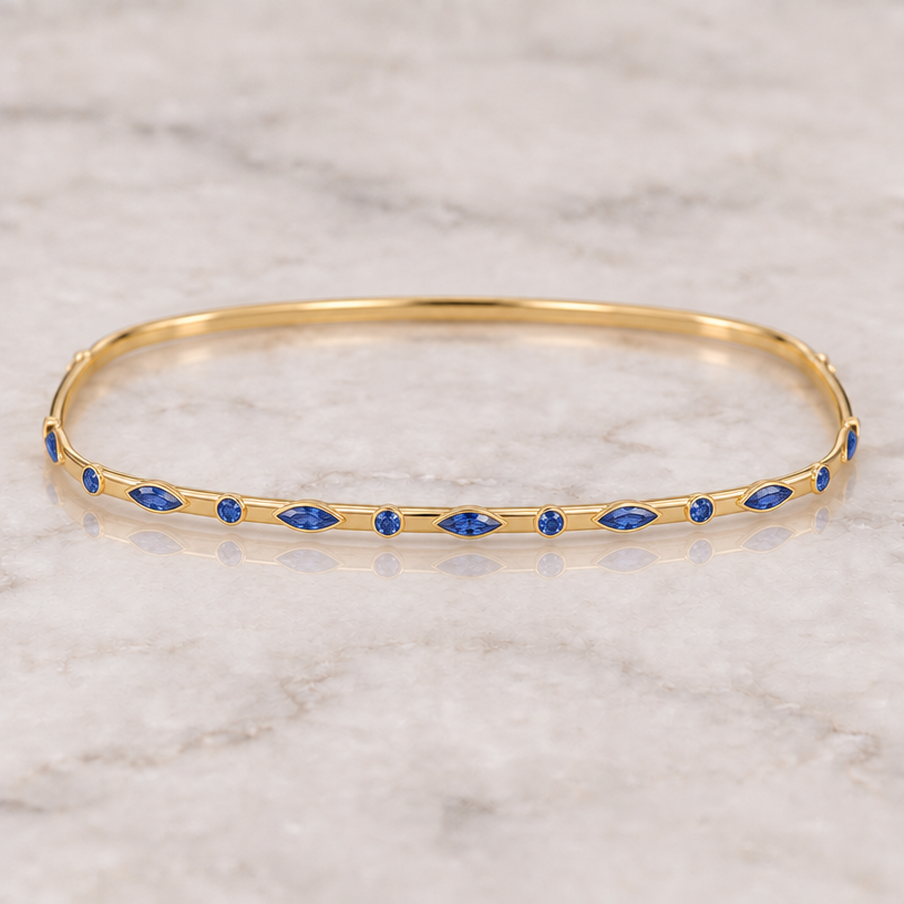 DO NOT CHANGE THE OVERALL SIZE OR PROPORTIONS OF THE BRACELET. KEEP IT EXTREMELY THIN, DAINTY AND DELICATE.
The current edit is incorrect because the gold band became too wide and the gemstones became large, colorful decorative shapes. Reverse those changes.
Keep the bracelet as a very thin, delicate, continuous 18K yellow-gold bangle, similar in overall thinness to the previous version. The bracelet must remain a normal elegant oval/circular bracelet around the wrist.
When I say I want the gold more rectangular, I am NOT referring to the overall shape of the bracelet and I am NOT asking you to make the band wider. I mean ONLY the tiny gold band's profile and edges: instead of looking like a rounded cylindrical wire, make the narrow gold band look like a thin flat ribbon of gold with crisp straight upper and lower edges. The front-facing gold surface should be narrow and flat. Think thin flat gold strip, NOT round wire and NOT a wide Cartier-style bangle.
REDUCE THE WIDTH OF THE GOLD BAND SIGNIFICANTLY from the current image. It should be approximately HALF of its current vertical width.
Now change the gemstones completely. REMOVE ALL pink, purple, green, yellow, turquoise and multicolored stones. ONLY USE BLUE GEMSTONES.
Use a sophisticated repeating sequence of deep sapphire-blue round stones and elongated marquise/navette blue stones. Keep the color consistent: rich, luminous sapphire blue with realistic icy highlights from the facets.
The gemstones should be larger than they were in the earlier tiny-stone version, but NOT chunky like the current image. I want a delicate middle size: clearly visible and important, but still fine-jewelry proportions.
Make the marquise gemstones long, narrow and sharply pointed, approximately 2–2.5 times longer than they are wide. They must look elegant and elongated rather than oval or bulky.
Make the round blue stones smaller than the marquise stones and alternate them in a precise repeating pattern:
small round sapphir
DO NOT CHANGE THE OVERALL SIZE OR PROPORTIONS OF THE BRACELET. KEEP IT EXTREMELY THIN, DAINTY AND DELICATE.
The current edit is incorrect because the gold band became too wide and the gemstones became large, colorful decorative shapes. Reverse those changes.
Keep the bracelet as a very thin, delicate, continuous 18K yellow-gold bangle, similar in overall thinness to the previous version. The bracelet must remain a normal elegant oval/circular bracelet around the wrist.
When I say I want the gold more rectangular, I am NOT referring to the overall shape of the bracelet and I am NOT asking you to make the band wider. I mean ONLY the tiny gold band's profile and edges: instead of looking like a rounded cylindrical wire, make the narrow gold band look like a thin flat ribbon of gold with crisp straight upper and lower edges. The front-facing gold surface should be narrow and flat. Think thin flat gold strip, NOT round wire and NOT a wide Cartier-style bangle.
REDUCE THE WIDTH OF THE GOLD BAND SIGNIFICANTLY from the current image. It should be approximately HALF of its current vertical width.
Now change the gemstones completely. REMOVE ALL pink, purple, green, yellow, turquoise and multicolored stones. ONLY USE BLUE GEMSTONES.
Use a sophisticated repeating sequence of deep sapphire-blue round stones and elongated marquise/navette blue stones. Keep the color consistent: rich, luminous sapphire blue with realistic icy highlights from the facets.
The gemstones should be larger than they were in the earlier tiny-stone version, but NOT chunky like the current image. I want a delicate middle size: clearly visible and important, but still fine-jewelry proportions.
Make the marquise gemstones long, narrow and sharply pointed, approximately 2–2.5 times longer than they are wide. They must look elegant and elongated rather than oval or bulky.
Make the round blue stones smaller than the marquise stones and alternate them in a precise repeating pattern:
small round sapphir
