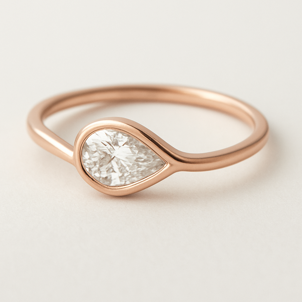 A delicate pinky ring crafted in rose gold, featuring a 0.50-carat pear-shaped diamond set in a smooth bezel setting. The diamond is tilted gently to the left, forming a paisley-inspired curve that expresses feminine Yin energy — soft, flowing, and intuitive. The polished rose gold band enhances the gentle movement and organic harmony of the design, creating a graceful balance of elegance and inner strength. 
