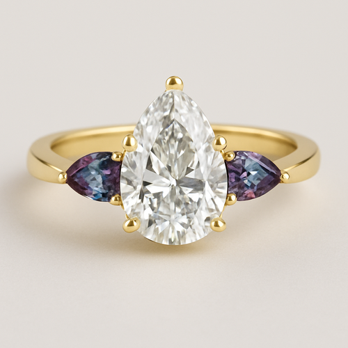 2 carat pear cut diamond with with claw prongs and marquise shaped alexandrite side stones set in a yellow flared shank 