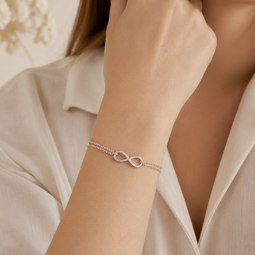 Jewelry photoshoot (worn)
Show the jewelry piece from the image worn by an elegant model in a professional editorial photograph, soft studio lighting. Reproduce the jewelry's exact design, metal, stones and details faithfully. Photorealistic, no text. Additional instructions: "Close-up beauty/editorial photo of a woman's wrist and hand, fair light skin tone, gently relaxed pose (resting on a soft surface or lightly touching her face/collarbone). Soft, warm neutral studio background (beige/cream tones), softly blurred, shallow depth of field.
She wears a delicate sterling silver chain bracelet featuring a small round bezel-set cubic zirconia stone on one side of the chain and a small sideways cross charm on the other side, connected by a fine cable chain.
METAL FINISH: the sterling silver must be rhodium-plated — bright, cool-white, and reflective with a polished mirror-like shine, not dull or matte. The metal should catch light naturally and sparkle realistically, without looking overly glossy, plastic, or artificially glowing.
SKIN REALISM REQUIREMENT: skin must look completely natural and photorealistic — fair, light skin tone to enhance the contrast and shine of the silver, with visible fine skin texture, natural pores, subtle imperfections. Avoid any smooth, plastic, airbrushed, CGI, or overly retouched look. Lighting soft and warm, casting natural gentle shadows.
STRICT SIZE REQUIREMENT: the bracelet must stay true to real-life scale, fine and delicate — the round stone approximately 0.6cm, the cross charm small and slim, both proportionate to the wrist. Do not enlarge or oversize.
BRACELET POSITION: the chain drapes naturally around the wrist, with the round stone and cross charm both visible and facing forward, sitting flat against the skin.
Close-up beauty/editorial photo of a woman's wrist and hand, fair light skin tone, gently relaxed pose (resting on a soft surface or lightly touching her face/collarbone). Soft, warm neutral studio background (beige/cream tones), softly blurred, shallow depth of field.
She wears a delicate sterling silver double-chain bracelet featuring a small infinity symbol charm, partially lined with sparkling pavé cubic zirconia stones on one side, connected by two fine parallel cable chains.
METAL FINISH: the sterling silver must be rhodium-plated — bright, cool-white, and reflective with a polished mirror-like shine, not dull or matte. The metal should catch light naturally and sparkle realistically, without looking overly glossy, plastic, or artificially glowing.
SKIN REALISM REQUIREMENT: skin must look completely natural and photorealistic — fair, light skin tone to enhance the contrast and shine of the silver, with visible fine skin texture, natural pores, subtle imperfections. Avoid any smooth, plastic, airbrushed, CGI, or overly retouched look. Lighting soft and warm, casting natural gentle shadows.
STRICT SIZE REQUIREMENT: the bracelet must stay true to real-life scale, fine and delicate — the infinity charm small and slim, proportionate to the wrist, double chain thin and dainty. Do not enlarge or oversize.
BRACELET POSITION: the double chain drapes naturally around the wrist, with the infinity charm centered and facing forward, sitting flat against the skin.
Mood: elegant, minimal, intimate — high-end jewelry brand photography style, sharp focus on the bracelet while keeping the composition natural and soft..