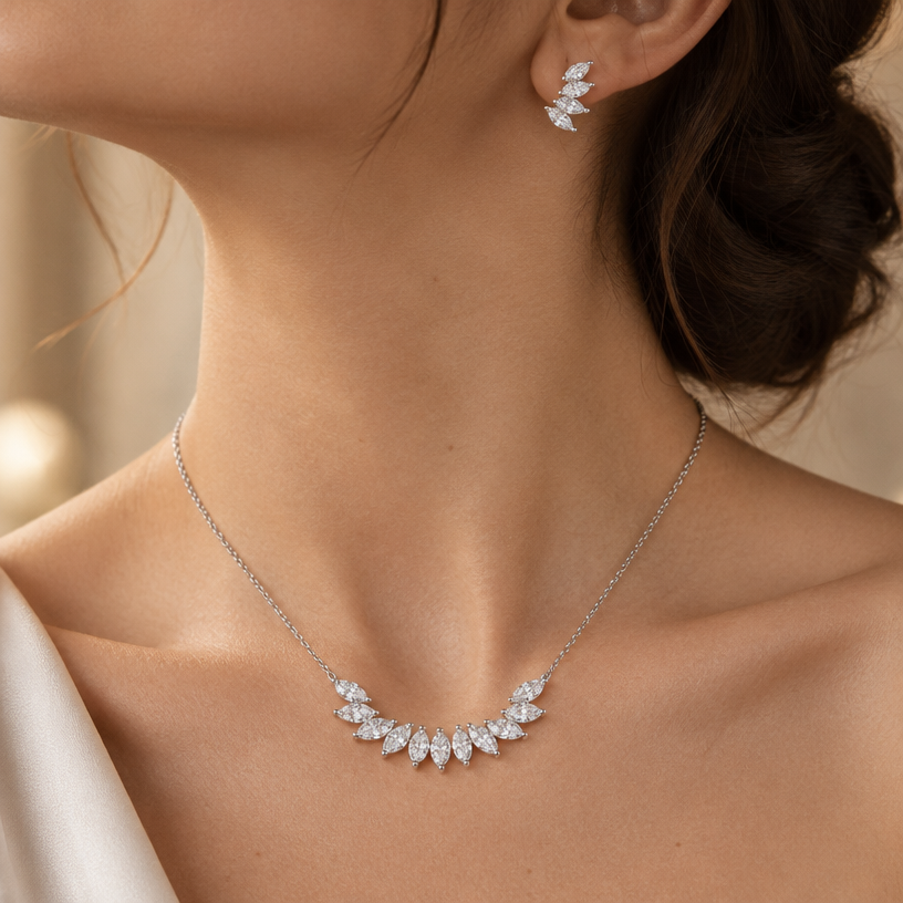 Jewelry photoshoot (worn)
Show the jewelry piece from the image worn by an elegant model in a professional editorial photograph, soft studio lighting. Reproduce the jewelry's exact design, metal, stones and details faithfully. Photorealistic, no text. Additional instructions: Close-up editorial jewelry photo of a woman's neck, collarbone, ear, and upper chest, cropped so the face is fully out of frame. She wears soft, elegant clothing, only a small part of the fabric visible at the edge of the frame.
VARY THE POSE: do not repeat the same head tilt, shoulder position, or framing as previous generations. Use natural variations such as: head turned left or right, chin slightly up or down, one shoulder raised or relaxed, hair swept to either side or tucked back, camera angle shifted slightly higher or lower. Keep the framing tight on the neck, collarbone, and ear (face always out of frame), but make the pose feel distinct and natural.
She wears a sterling silver necklace featuring a cluster of marquise-cut clear cubic zirconia stones arranged in a leaf/petal fan pattern at the center of the chain, and a matching pair of marquise-cut cubic zirconia cluster stud earrings in the same leaf/petal fan design.
METAL FINISH: the sterling silver must be rhodium-plated — bright, cool-white, and reflective with a polished mirror-like shine, not dull or matte. The metal should catch light naturally, without looking overly glossy, plastic, or artificially glowing.
STONE DETAIL: the marquise-cut cubic zirconia stones must be clear, sparkling, and perfectly faceted, each with sharp pointed oval facets, catching light realistically with natural brilliance, arranged in a fanned cluster resembling small crystal leaves.
STRICT SIZE REQUIREMENT: the necklace cluster must be exactly 3cm width, and each earring exactly 1.4cm height x 0.6cm width, true to real-life scale against the neck, collarbone, and ear. Do not enlarge or oversize — the pieces should look delicate and proportionate.
SKIN REALISM REQUIREMENT: skin must look completely natural and photorealistic — visible fine skin texture, natural pores, subtle imperfections, soft even tone. Avoid any smooth, plastic, airbrushed, CGI, or overly retouched look. Lighting soft and warm, casting natural gentle shadows.
CHAIN AND PENDANT POSITION: fine cable chain draping naturally in a soft V-shape along the collarbone, with the marquise cluster centered at the lowest point of the chain, symmetric and facing forward. The stud earrings sit naturally and securely on the earlobes, cluster pattern facing forward and clearly visible.
Background softly blurred, warm and neutral, shallow depth of field. Mood: elegant, minimal, intimate — natural high-end jewelry brand photography style, face not shown, jewelry clearly and accurately rendered in true detail and correct scale..