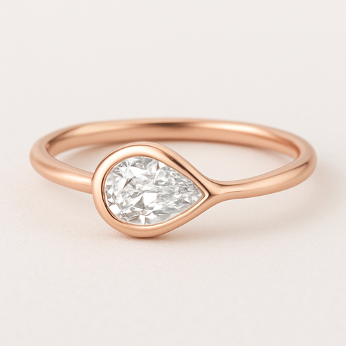 A delicate rose gold pinky ring featuring a 0.50-carat pear-shaped diamond set in a smooth bezel setting. The diamond is gently tilted to the left, creating a soft paisley-inspired curve that radiates feminine Yin energy — graceful, flowing, intuitive, and serene. The polished rose gold band enhances the gentle movement and balance of the design, symbolizing elegance, emotional depth, and the beauty of lunar energy.  