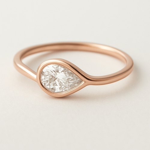 A delicate pinky ring crafted in rose gold, featuring a 0.50-carat pear-shaped diamond set in a smooth bezel setting. The diamond is tilted gently to the left, forming a paisley-inspired curve that expresses feminine Yin energy — soft, flowing, and intuitive. The polished rose gold band enhances the gentle movement and organic harmony of the design, creating a graceful balance of elegance and inner strength. 