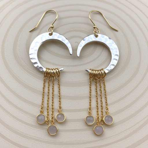 Серебряные серьги словно мятое серебро в форме полумесяца. Верхушка полумесяца крепится к застежке серьги.  От полумесяца идет три цепочки золотого цвета, у каждой на конце мелкий камушек лунный камень