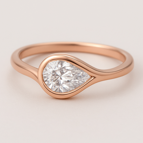 A refined and elegant rose gold ring featuring a pear-shaped diamond set in a smooth bezel setting. The diamond is tilted slightly to the side, creating a paisley-inspired shape reminiscent of a graceful flowing droplet. The rose gold band is sleek and polished, complementing the organic, curving silhouette of the stone. The design blends modern minimalism with a subtle artistic twist inspired by the Bandana paisley motif.