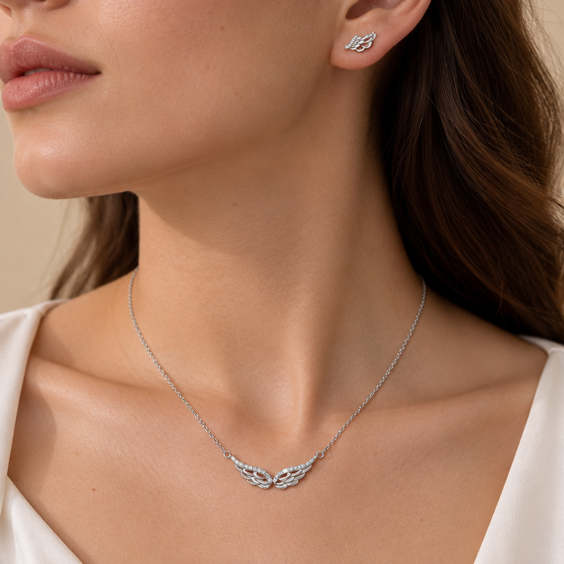 Jewelry photoshoot (worn)
Show the jewelry piece from the image worn by an elegant model in a professional editorial photograph, soft studio lighting. Reproduce the jewelry's exact design, metal, stones and details faithfully. Photorealistic, no text. Additional instructions: Close-up editorial jewelry photo of a woman's neck, collarbone, and ear, tightly cropped (chin, jaw, and lips partially in frame, head gently turned to the side). She wears a sterling silver angel wings pendant necklace and a matching angel wing stud earring, both featuring layered feather-textured wing details, with the top curved edge of the wings lined in sparkling pavé cubic zirconia stones and the lower feather layers left smooth polished silver.
METAL FINISH: the sterling silver must be rhodium-plated — bright, cool-white, and reflective with a polished mirror-like shine, not dull or matte. The metal should catch light naturally and sparkle realistically, without looking overly glossy, plastic, or artificially glowing.
SKIN REALISM REQUIREMENT: skin must look completely natural and photorealistic — visible fine skin texture, natural pores, subtle imperfections, soft even tone. Avoid any smooth, plastic, airbrushed, CGI, or overly retouched look. Lighting soft and warm, casting natural gentle shadows.
STRICT SIZE REQUIREMENT: the pendant must be exactly 3cm width, and the earring exactly 1.1cm width, true to real-life scale against the neck and ear — do not enlarge or oversize.
CHAIN AND PENDANT POSITION: fine cable chain draping naturally in a soft V-shape along the collarbone, with the double wing pendant hanging centered and horizontal, symmetric wings spreading outward, attached by two small jump rings at the top edges.
Background a warm blurred neutral tone (cream/beige), shallow depth of field. Mood: elegant, minimal, intimate — natural high-end jewelry brand photography style, matching the reference close-up shot..