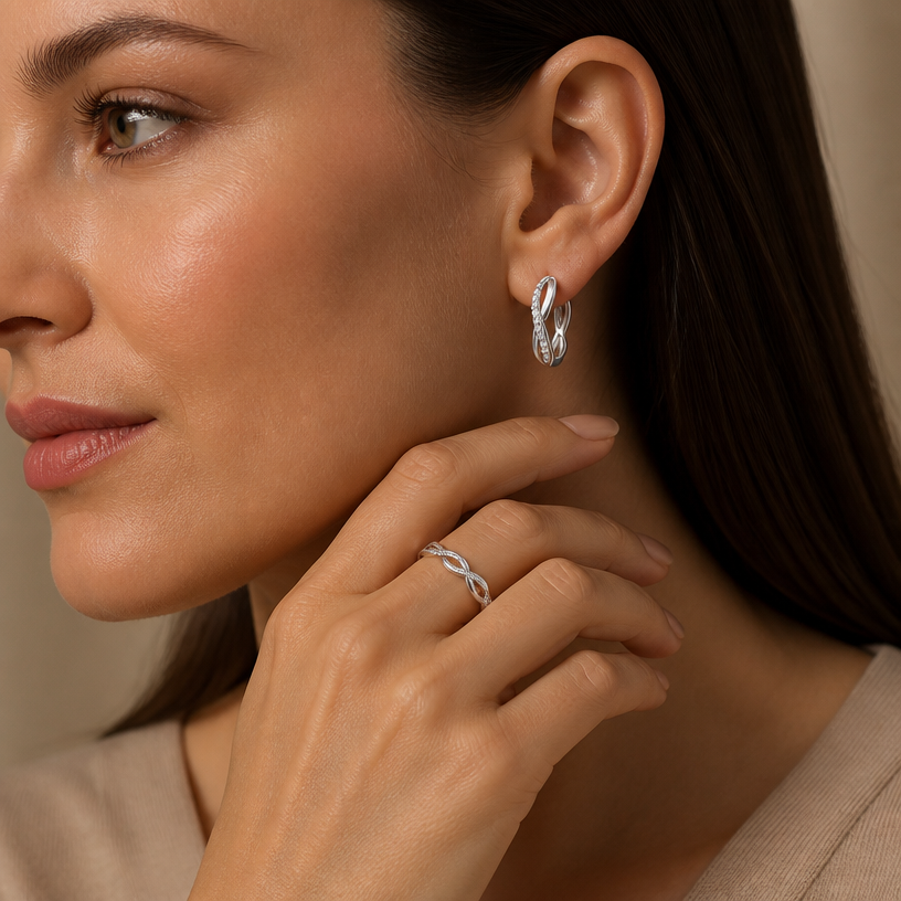 Jewelry photoshoot (worn)
Show the jewelry piece from the image worn by an elegant model in a professional editorial photograph, soft studio lighting. Reproduce the jewelry's exact design, metal, stones and details faithfully. Photorealistic, no text. Additional instructions: Close-up beauty/editorial photo of a woman's hand gently resting near her face and jawline, fingers relaxed and slightly curled, with her ear also visible and exposed (hair pulled back or tucked behind the ear). Head gently turned to show both the hand and the ear clearly in frame. Soft, warm neutral studio background (beige/cream tones), softly blurred, shallow depth of field.
She wears a sterling silver twisted infinity open cuff ring on her finger, and a matching sterling silver twisted infinity hoop earring, both featuring the same interwoven double-band design — one smooth polished band crossing over a second band fully lined with sparkling pavé cubic zirconia stones, forming a twisted braid-like pattern.
METAL FINISH: the sterling silver must be rhodium-plated — bright, cool-white, and reflective with a polished mirror-like shine, not dull or matte. The metal should catch light naturally and sparkle realistically, without looking overly glossy, plastic, or artificially glowing.
SKIN REALISM REQUIREMENT: skin must look completely natural and photorealistic — visible fine skin texture, natural pores, subtle imperfections, soft even tone, natural nails. Avoid any smooth, plastic, airbrushed, CGI, or overly retouched look. Lighting soft and warm, casting natural gentle shadows.
STRICT SIZE REQUIREMENT: both the ring and hoop earring must stay true to real-life scale — the ring sitting naturally on the finger (not oversized or bulky), and the earring at approximately 1.4cm height x 0.3cm band width against the ear.
JEWELRY POSITION: the ring sits naturally centered on the finger with the open twisted band visible; the earring hangs through the earlobe with the twisted pavé pattern facing forward, clearly visible.
Mood: elegant, minimal, intimate — high-end jewelry brand photography style, sharp focus on both the ring and earring while keeping the composition natural and soft..