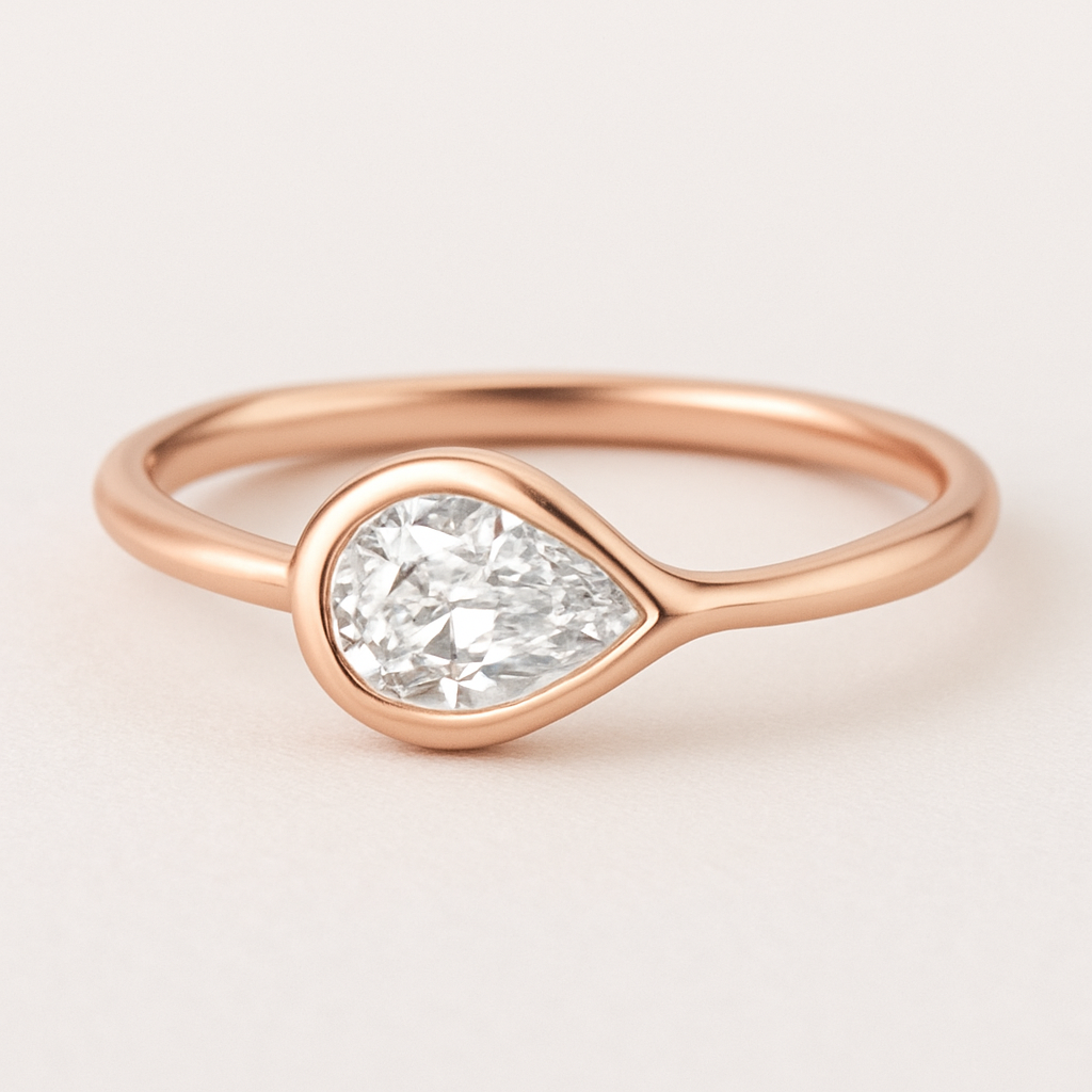 A delicate rose gold pinky ring featuring a 0.50-carat pear-shaped diamond set in a smooth bezel setting. The diamond is gently tilted to the left, creating a soft paisley-inspired curve that radiates feminine Yin energy — graceful, flowing, intuitive, and serene. The polished rose gold band enhances the gentle movement and balance of the design, symbolizing elegance, emotional depth, and the beauty of lunar energy.  